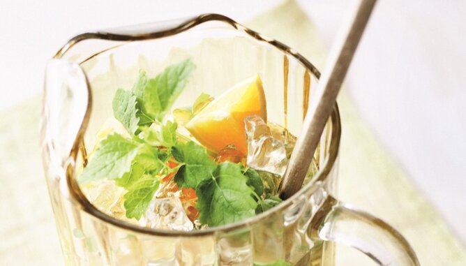 Auf dem Foto ist eine Karaffe mit Eistee Cocktail zu sehen. Darin sieht man eine Menge Eiswürfel, Minze und Zitornenstücke. | © SONNENTOR